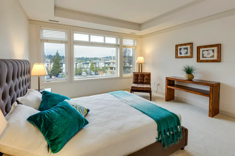 Reference photograph: a bedroom with a grey upholstered headboard and turquoise throw below broad windows.