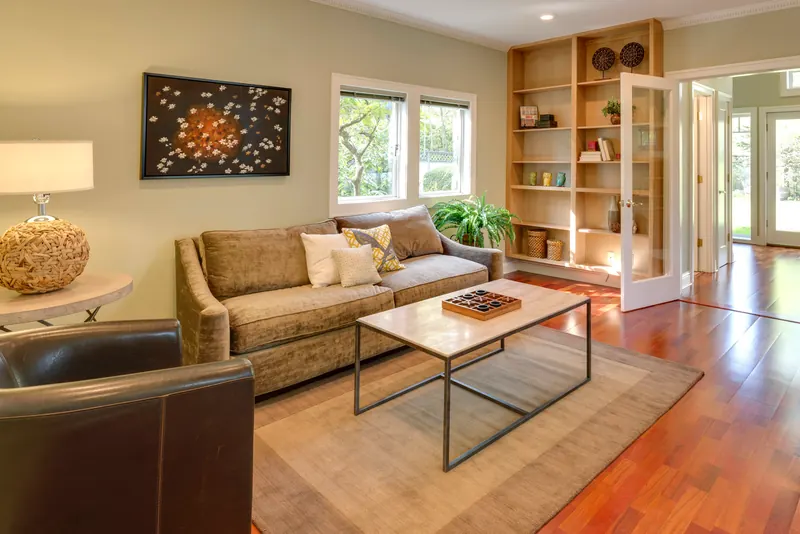 Reference photograph: a warm living room with a beige sofa, wood floor and open shelving.