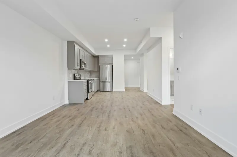 Reference photograph: an open unfurnished room looking back towards a compact grey kitchen.
