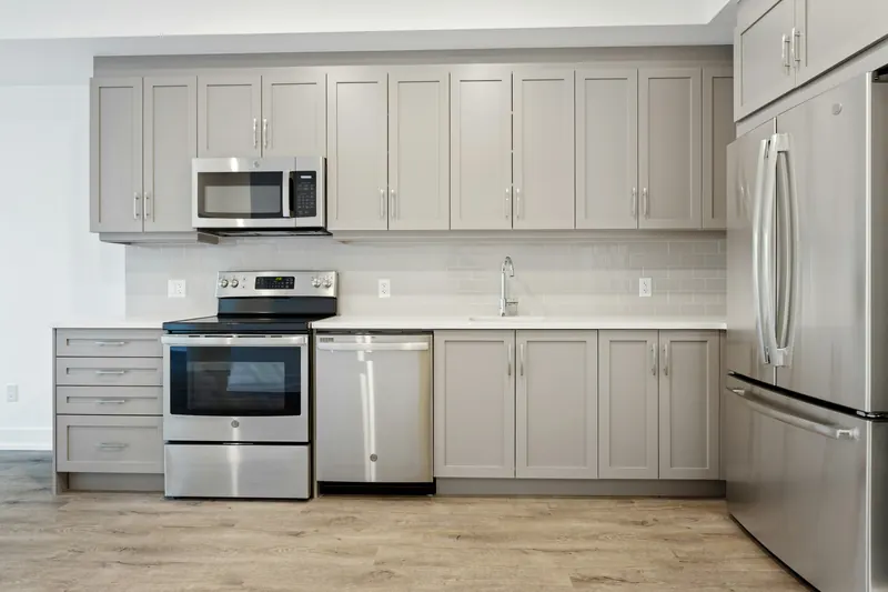 Reference photograph: a compact grey kitchen wall with a cooker, refrigerator and pale tiled splashback.