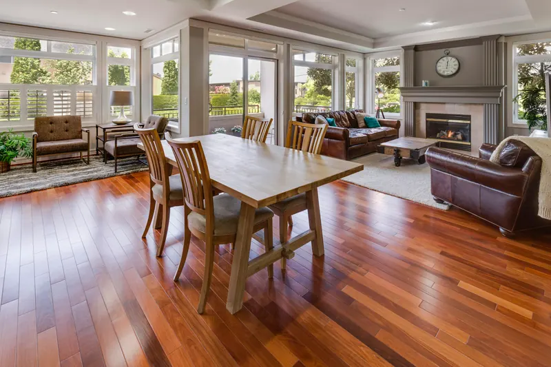 Reference photograph: a dining table and living area beneath broad windows facing greenery.
