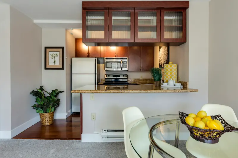 Reference photograph: a wood-fronted kitchen seen through a serving opening beside a glass dining table.