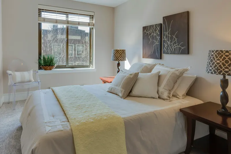 Reference photograph: a pale bedroom with patterned bedside lamps and a window behind the bed.