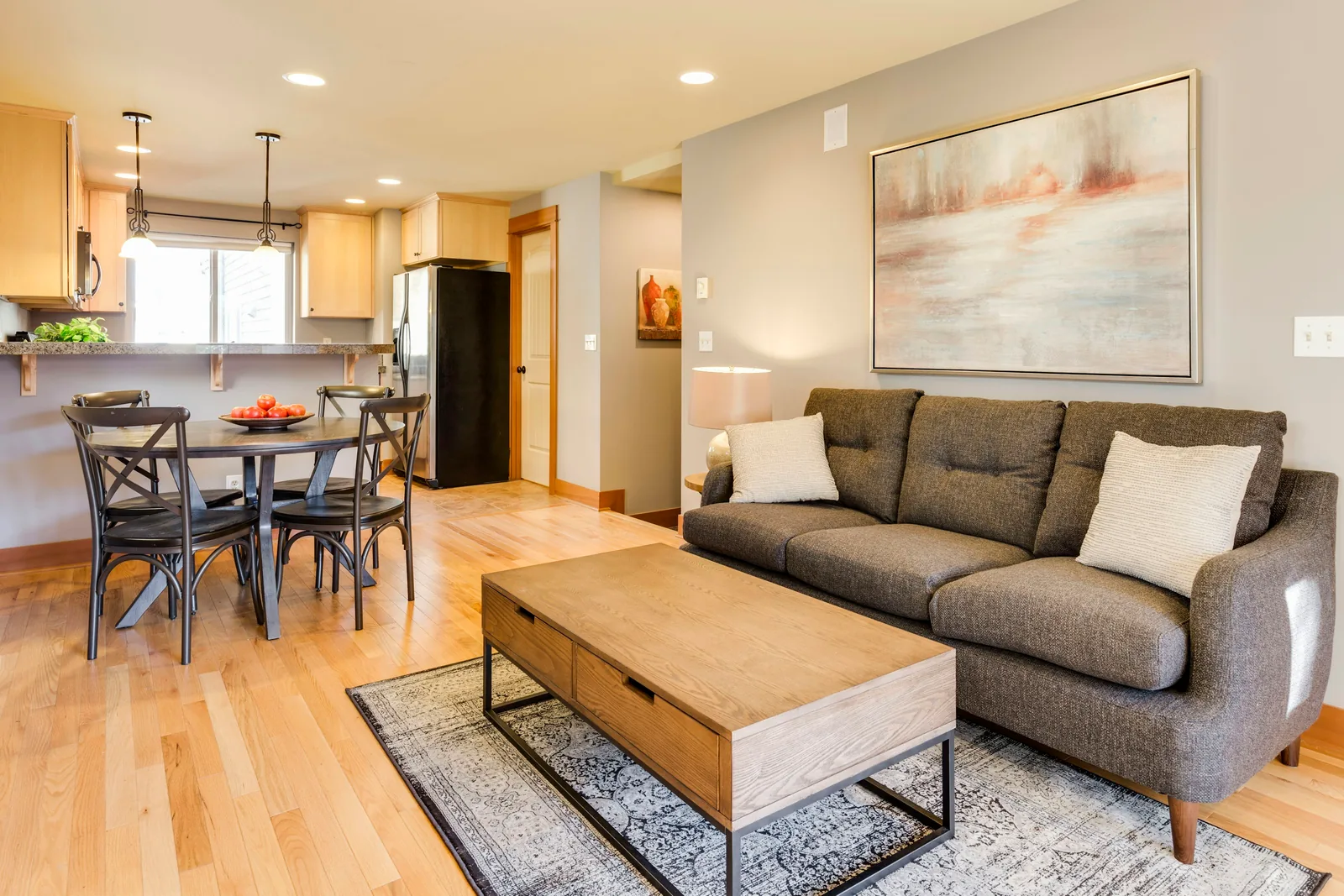 Reference photograph: a grey sofa and wood coffee table beside an open dining and kitchen space.