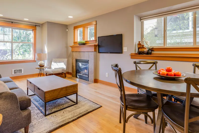Reference photograph: a round dining table beside a grey sofa, wood floor and dark fireplace surround.