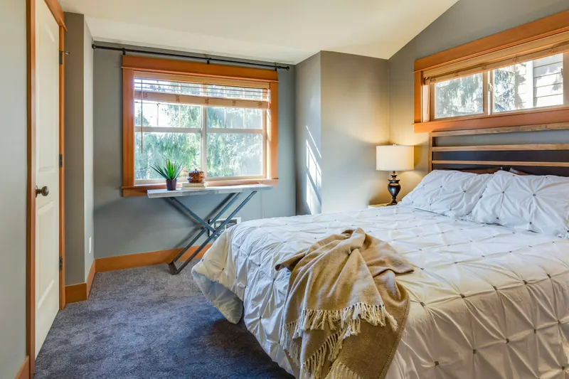 Reference photograph: a bedroom with wood-framed windows, pale bedding and a dark headboard.