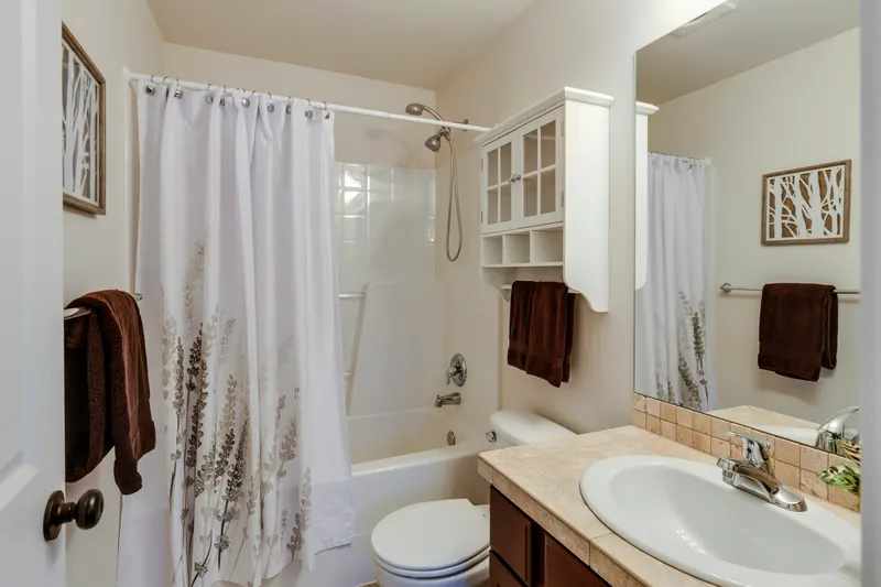 Reference photograph: a bathroom with a white bath, shower curtain and wood-fronted vanity.