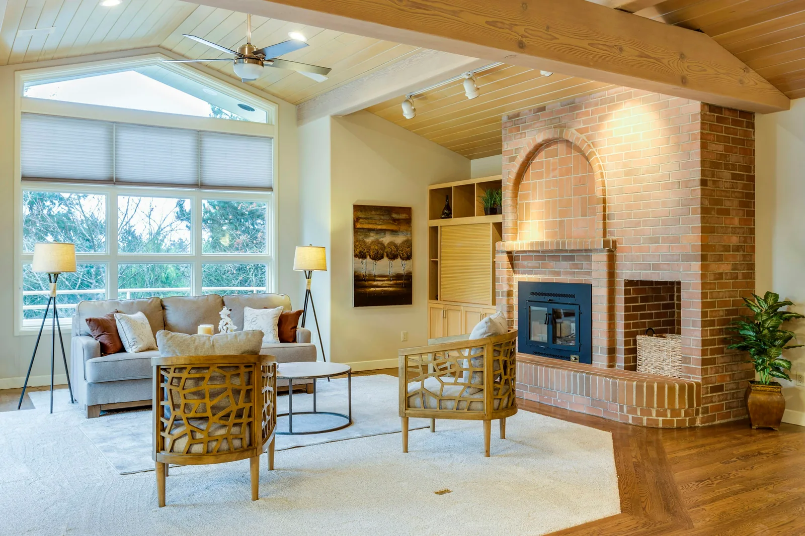 Reference photograph: a bright living room with a brick fireplace, pale seating and garden-facing glazing.