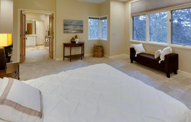 Reference photograph: a generous pale bedroom with a dark bench and windows on adjoining walls.