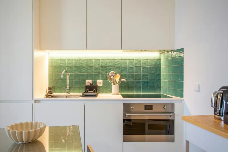 Reference photograph: a white kitchenette with a green tiled splashback and integrated oven.