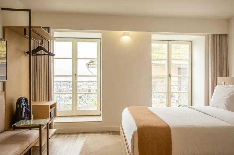 Reference photograph: a bed within a light studio room beside tall windows and a television unit.