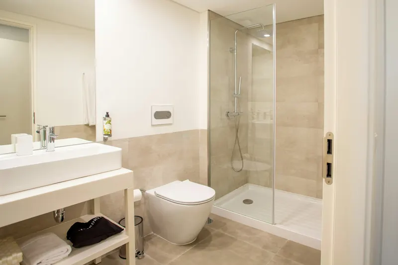 Reference photograph: a compact white and stone-coloured shower room with a glass screen.