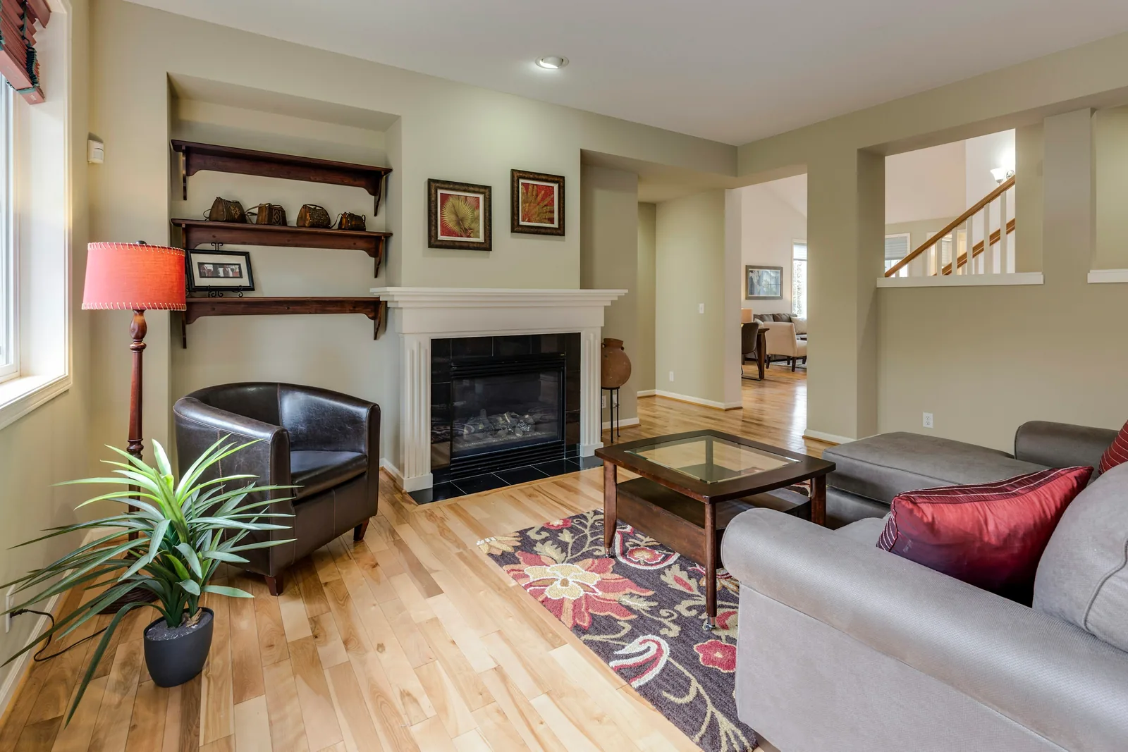 Reference photograph: a cosy living room with grey seating, red cushions and a dark fireplace.