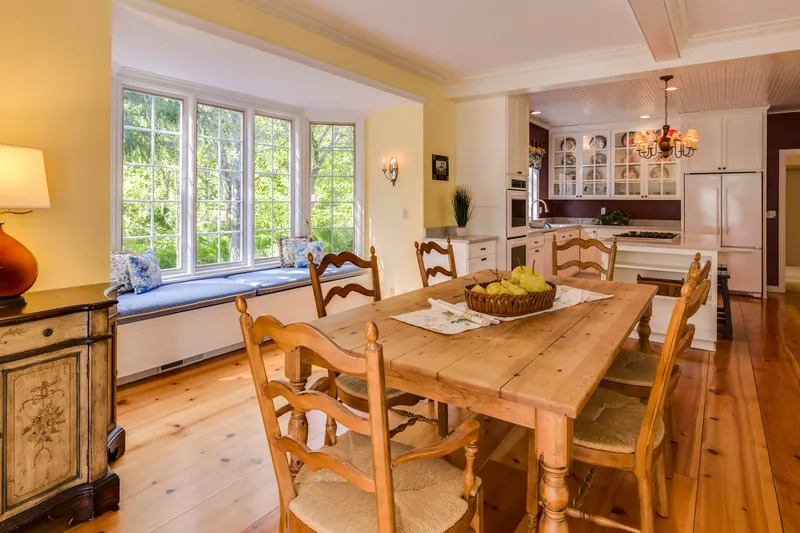 Reference photograph: a wood dining table beside tall windows and a bright kitchen.
