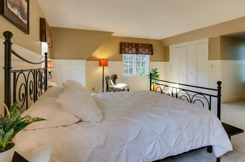 Reference photograph: a bedroom with a dark metal bed frame, pale bedding and warm lighting.