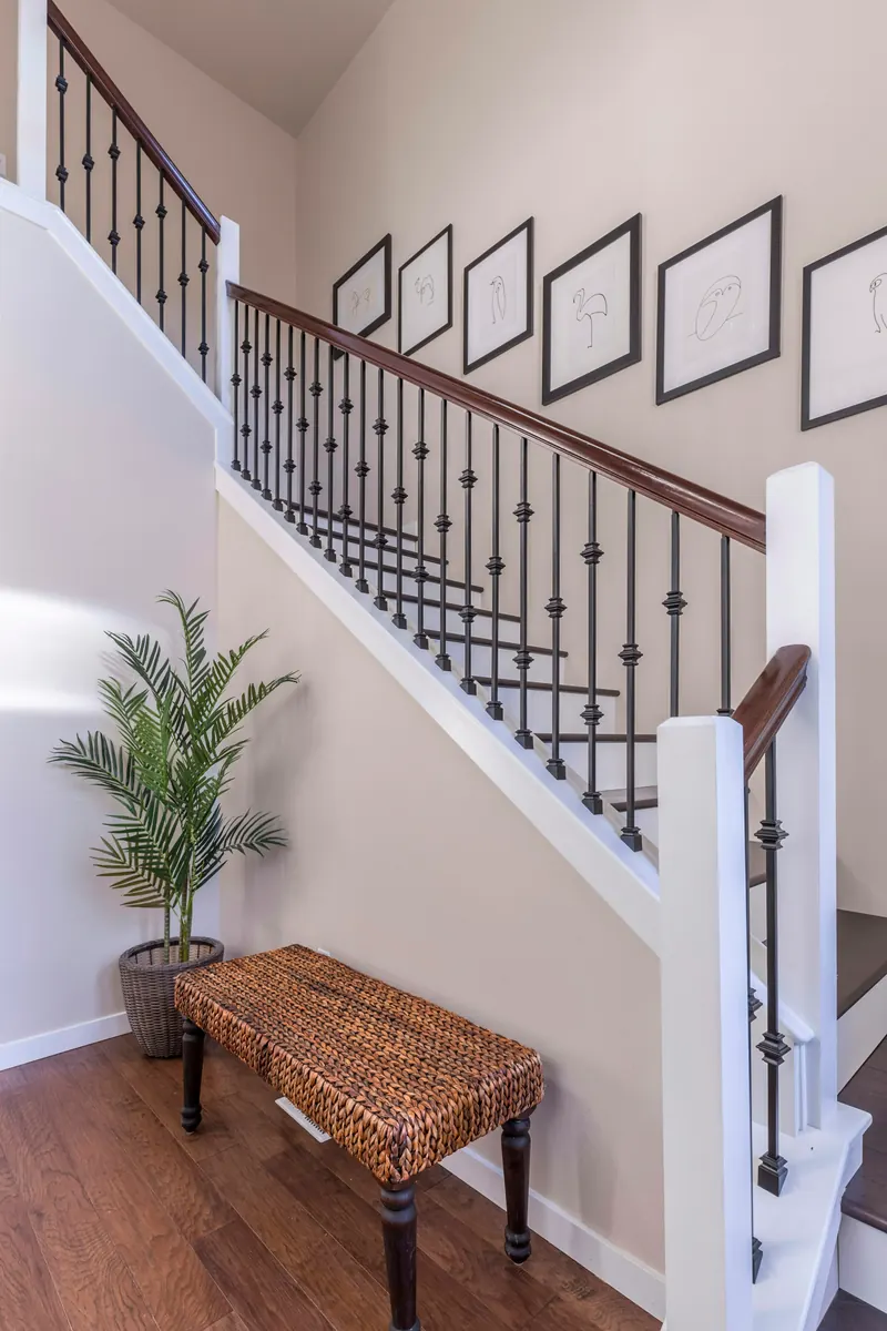 Reference photograph: a pale stair hall with dark balusters, framed pictures and a wood bench.
