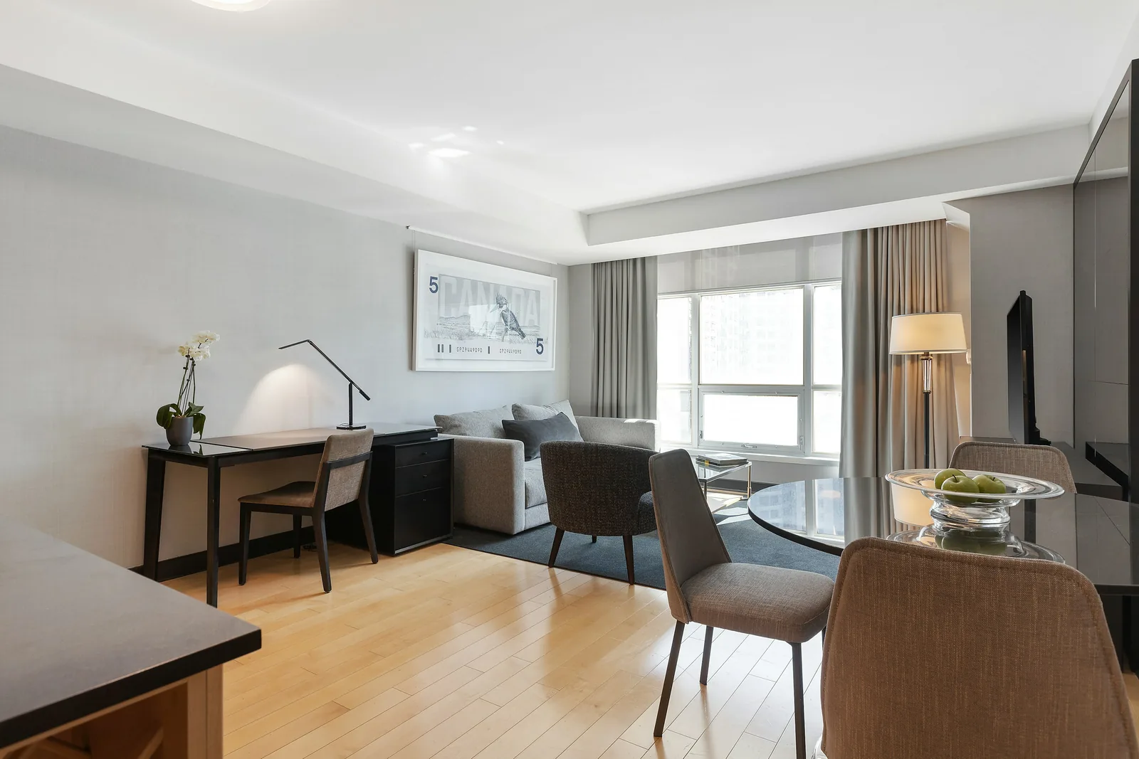 Reference photograph: a compact sitting and dining space with a dark desk, pale chairs and a curtained window.