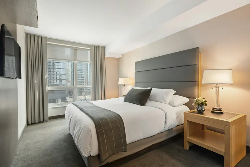 Reference photograph: a bedroom with a charcoal upholstered headboard, pale bedding and wood bedside tables.