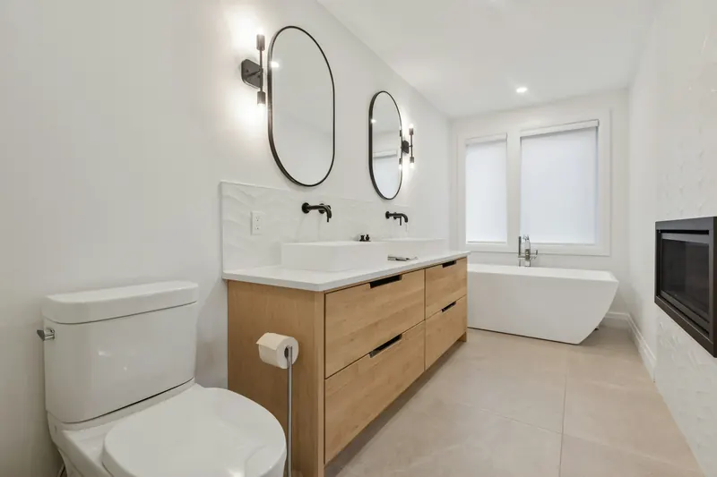Reference photograph: a light bathroom with a wood vanity, round mirrors and a freestanding bath.